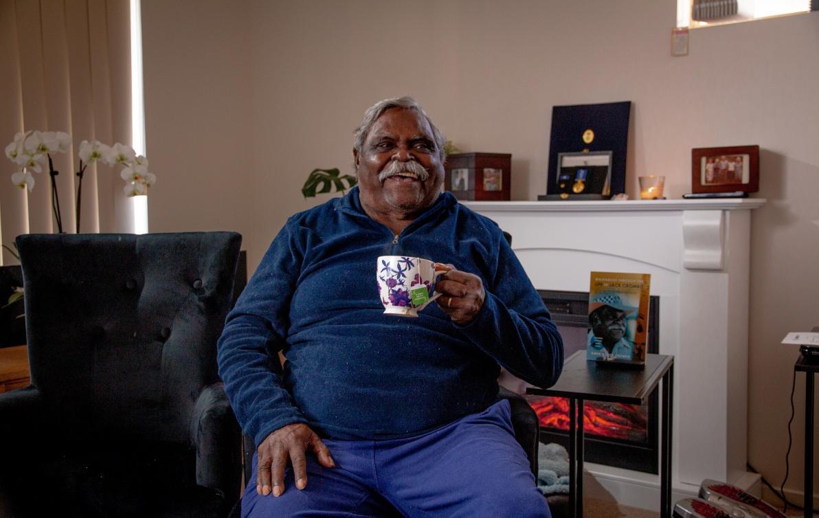 A man sitting in his living room holidng a coffee mug and smiling