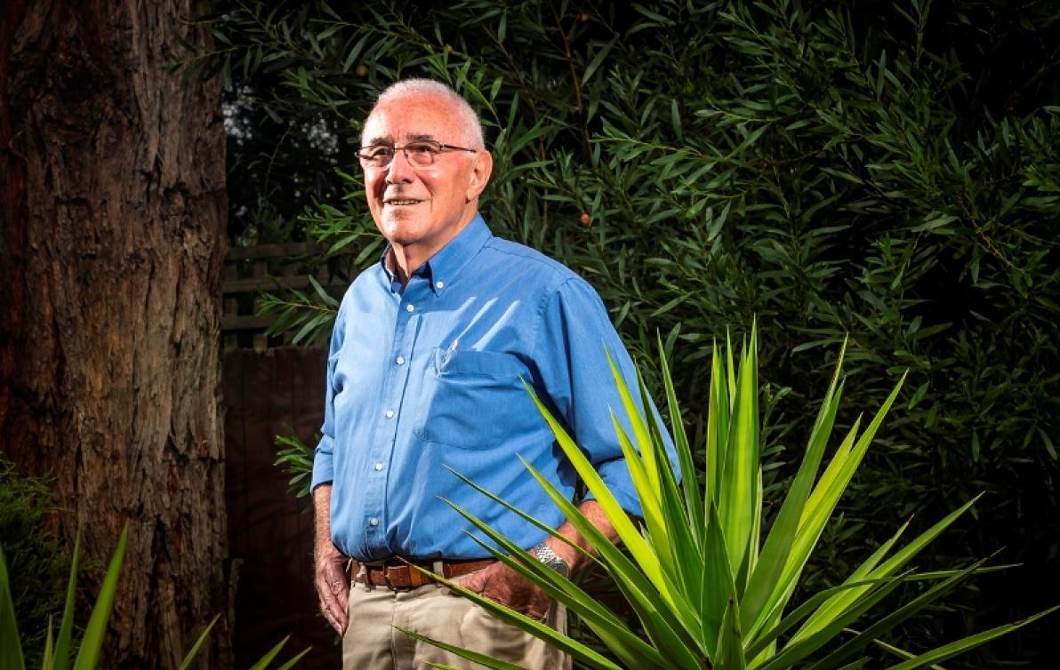 A man wearing a blue shirt standing in his garden with hands in pockets and smiling