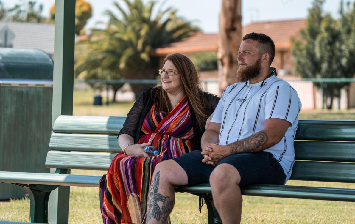 A man and woman sitting on a park bench on a sunny day.