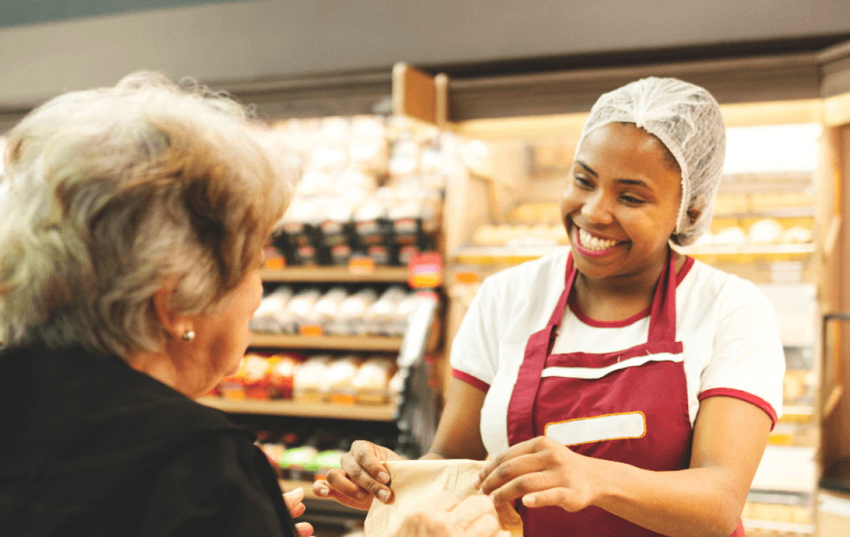 A smiling baker serves a customer.