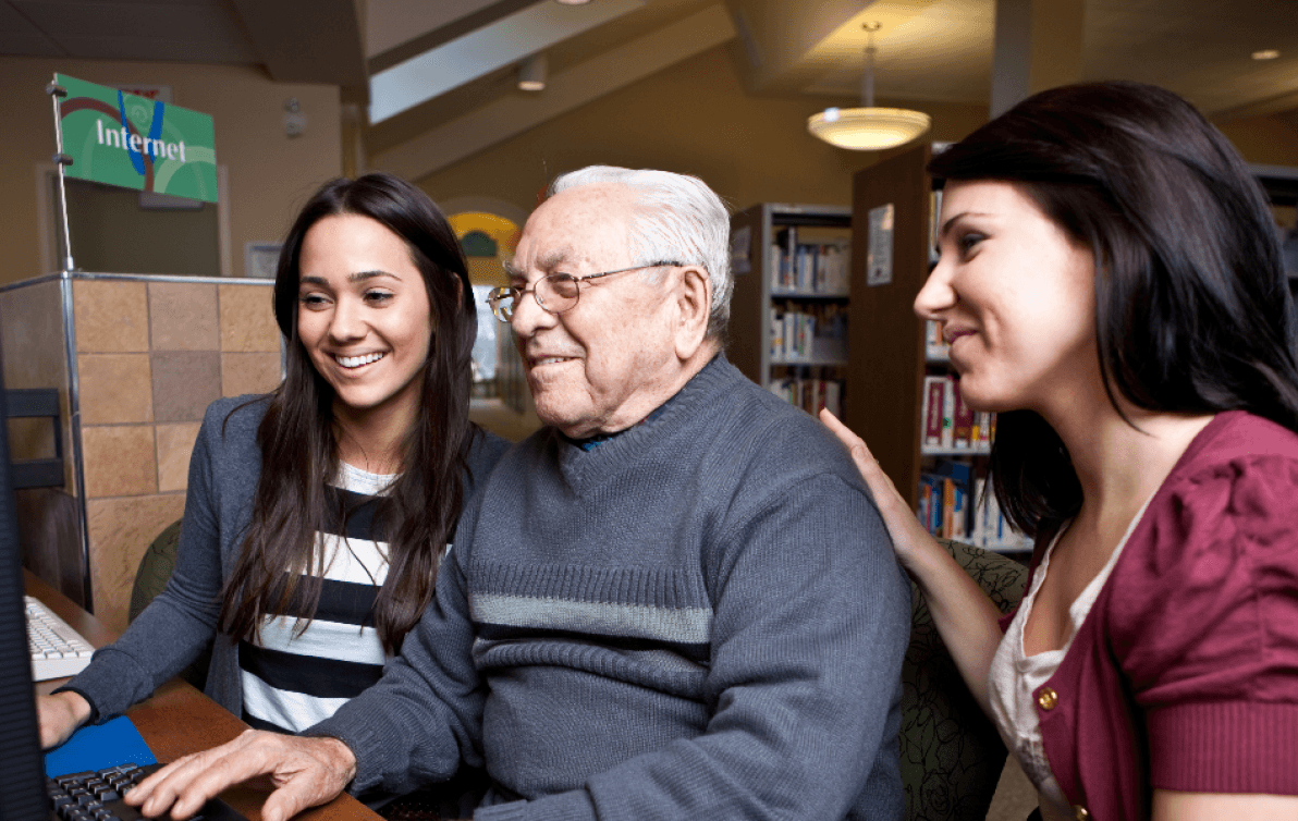 Two women and an older man use a computer at a council library.