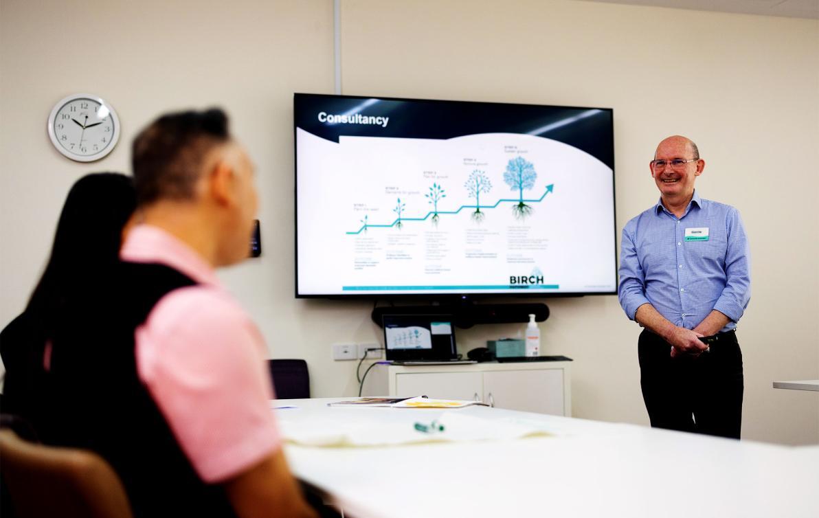 An office classroom with a smiling male presenting some training