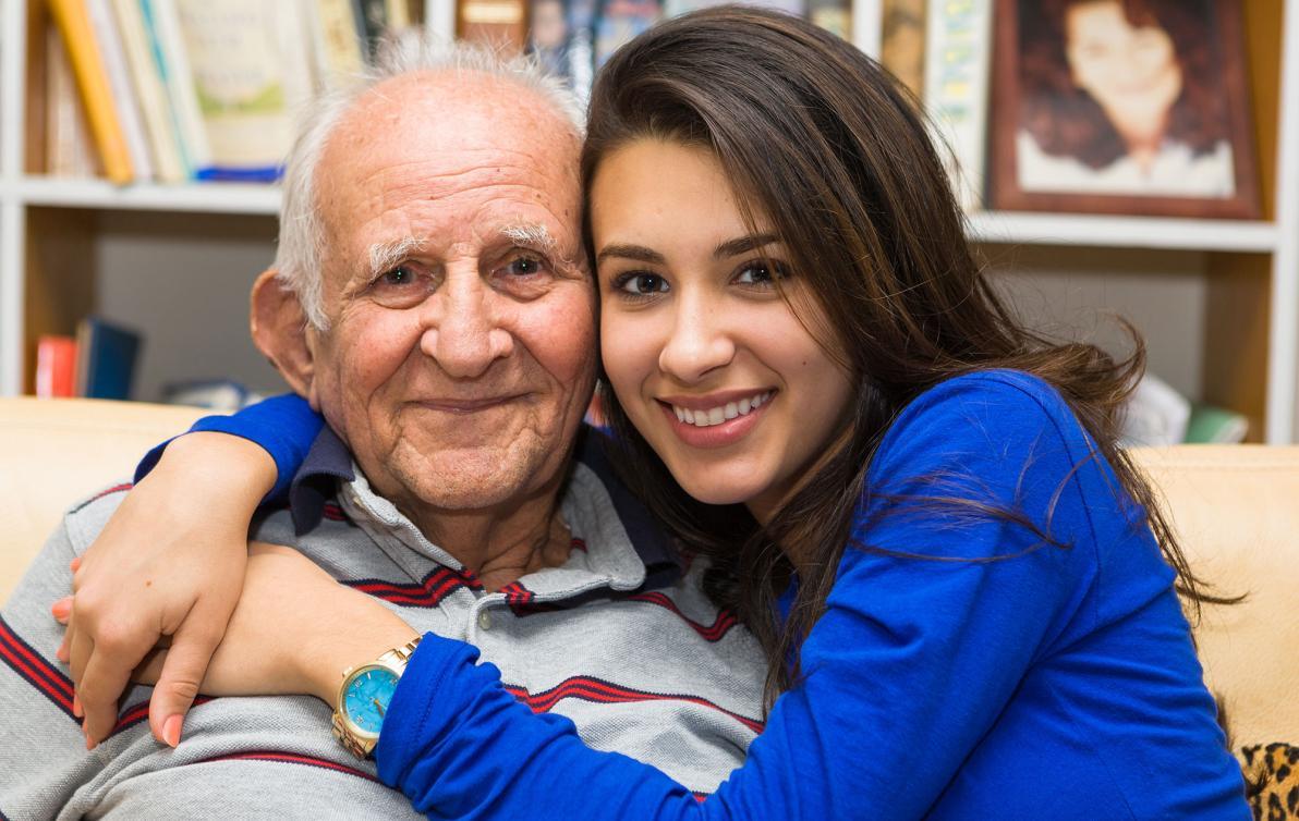 A younger female hugging an older male and both smiling at the camera