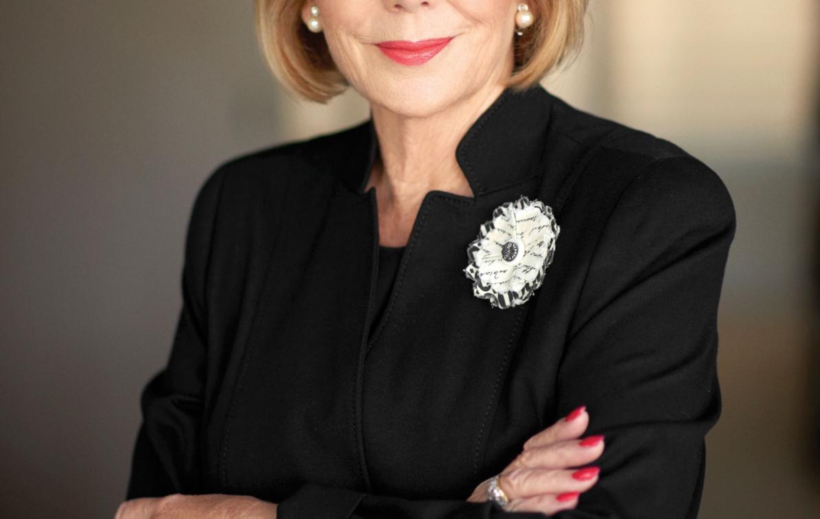 Ita Buttrose portrait wearing black clothing, smiling at the camera with arms crossed