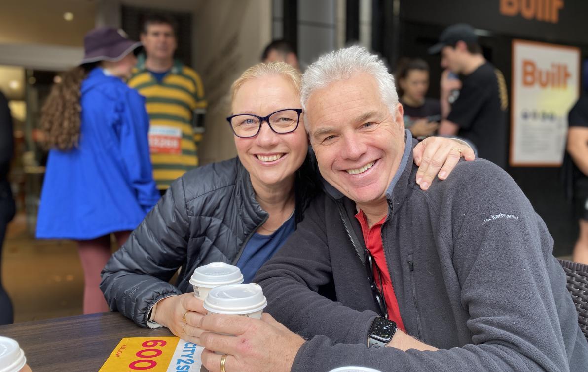 A man and woman sit together at an outdoor table with coffee cups