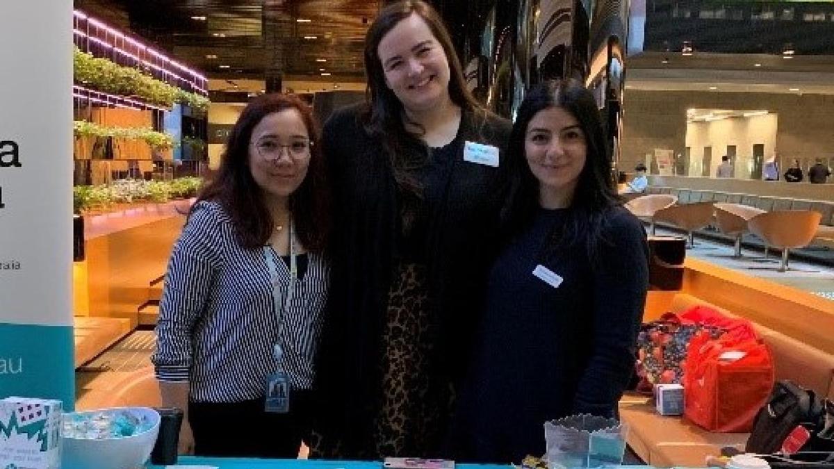 Dementia Australia employees stand in a large hall in front of a table with merchandise on it.