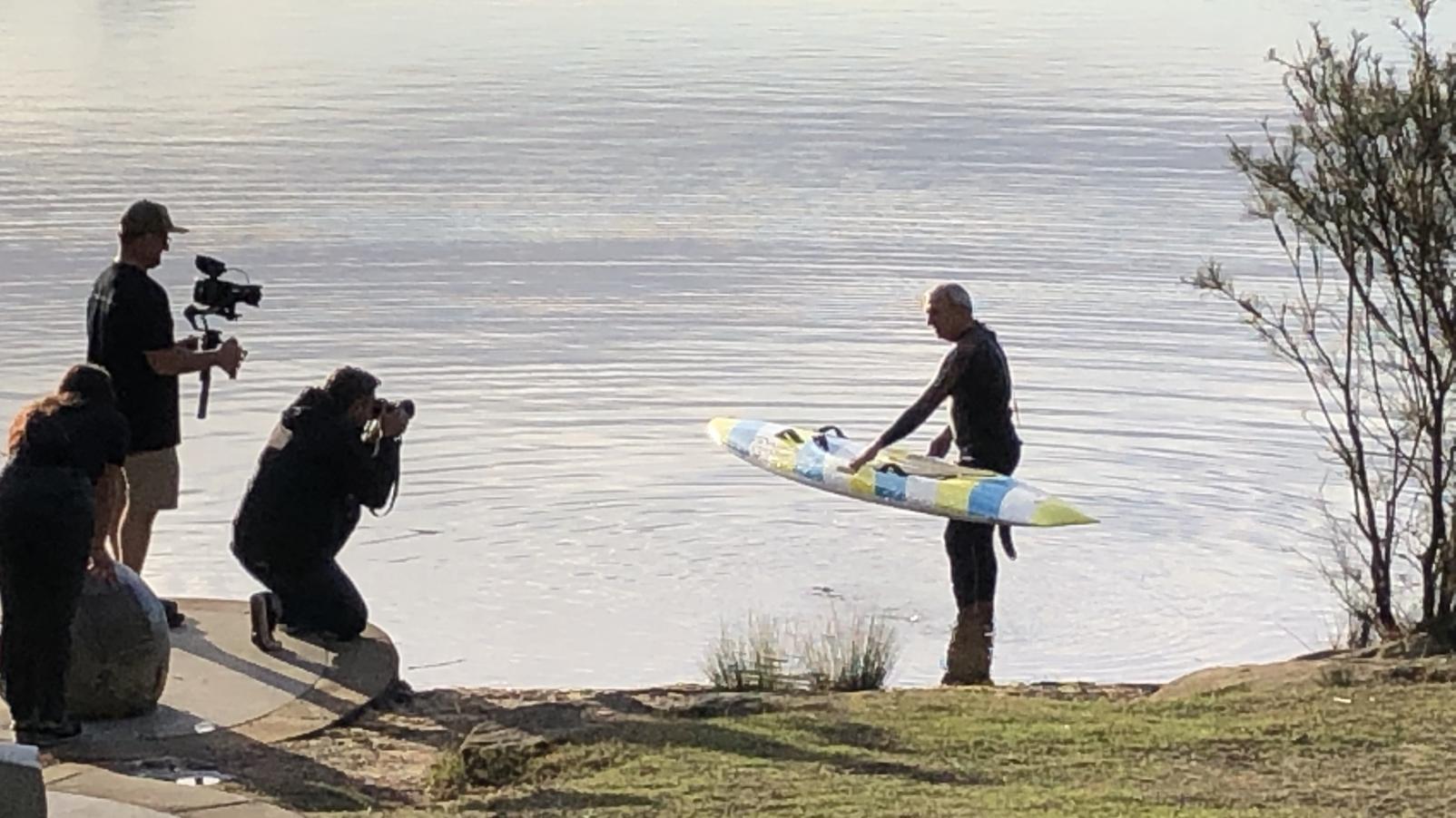 Dementia Advocate Bill Yeates holding a surfboard in Manly