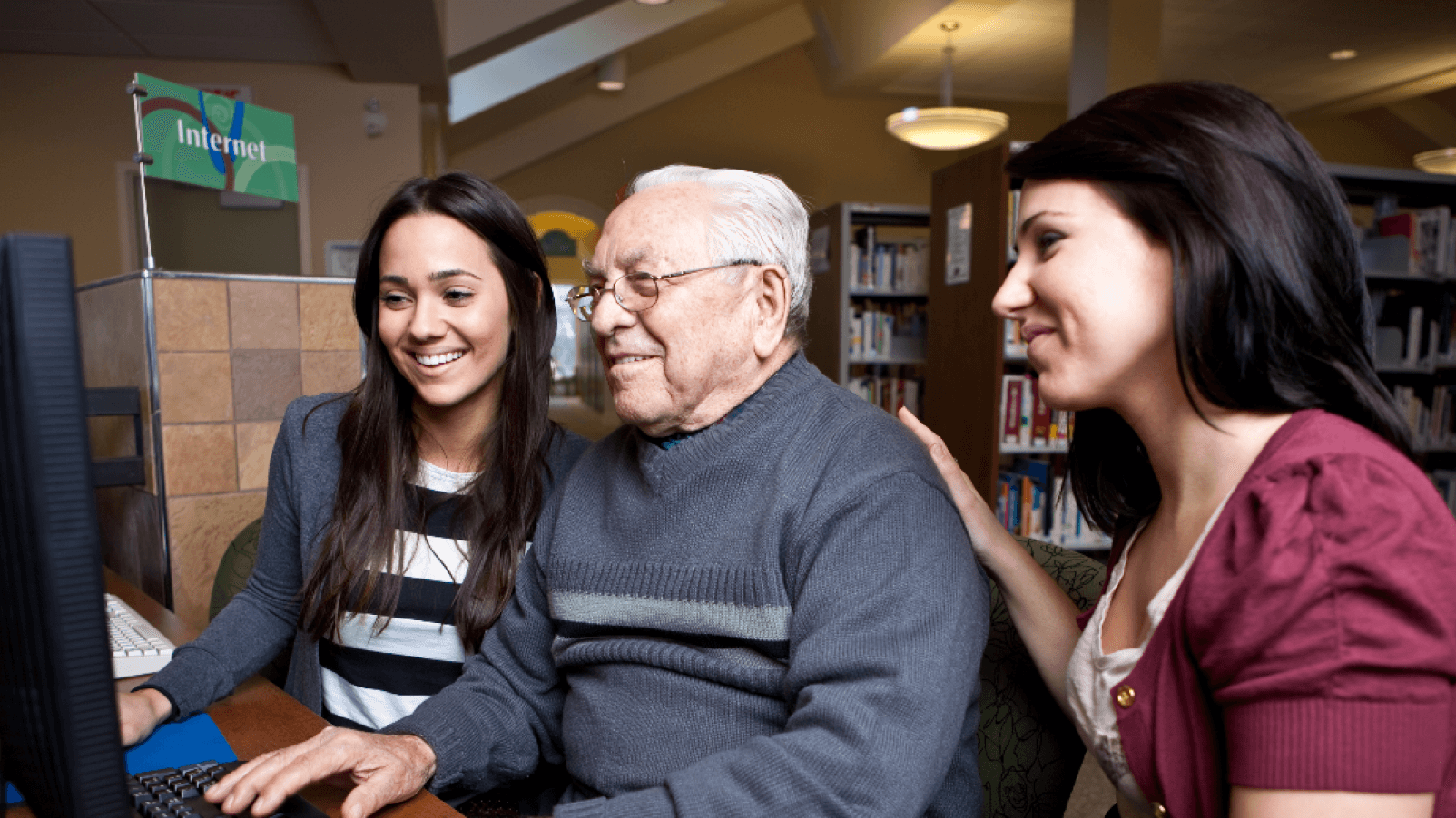 Two women and an older man use a computer at a council library.