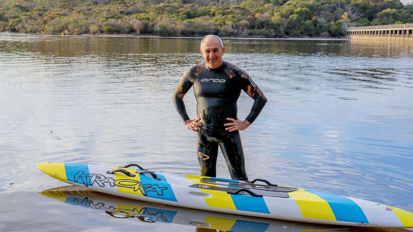 Dementia Advocate Bill in a wetsuit in front of a kayak in shallow water