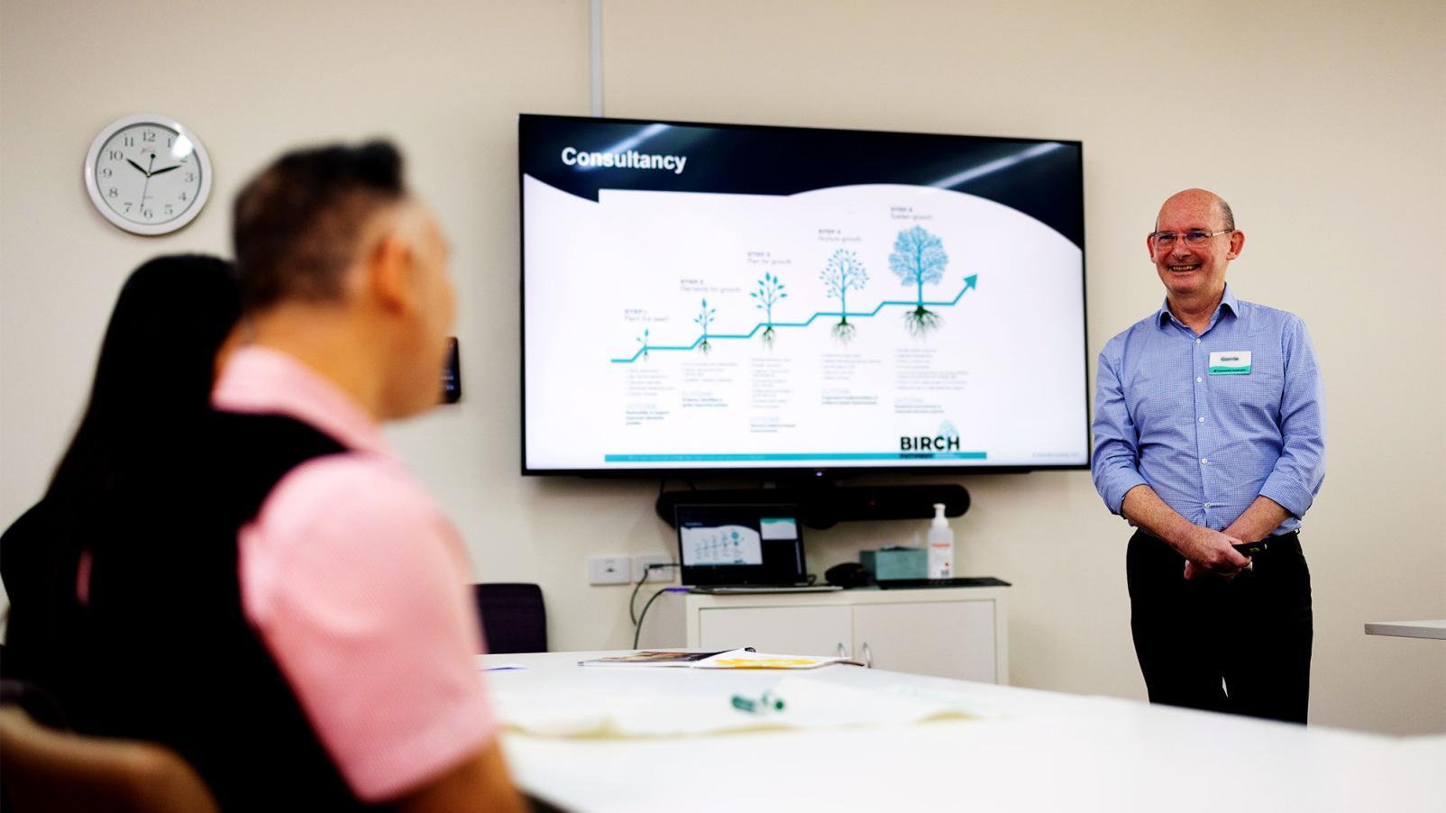 An office classroom with a smiling male presenting some training