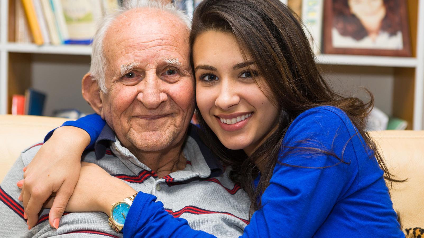 A younger female hugging an older male and both smiling at the camera