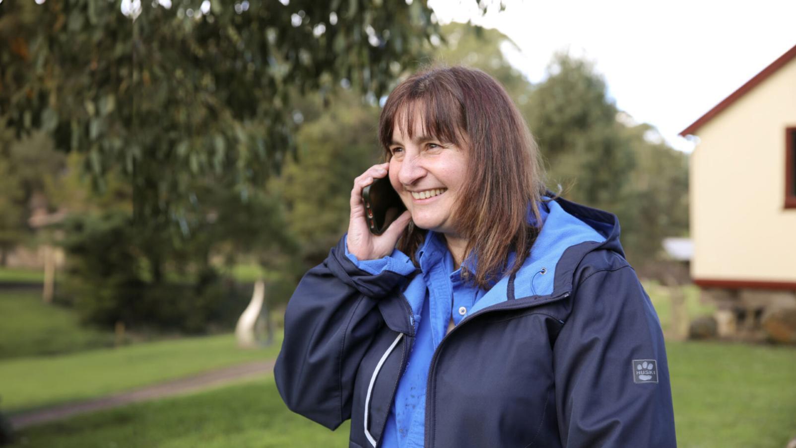 A woman wearing a blue jacket standing outside on her telephone talking to someone.