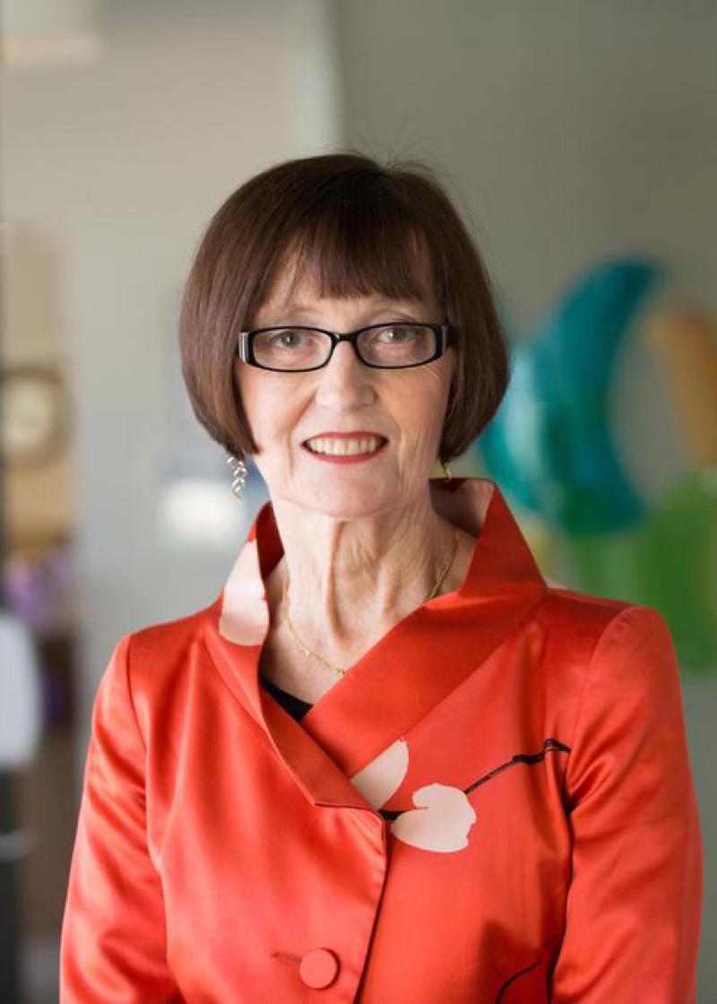 Christine Bryden looking at the camera, smiling and wearing glasses and a red jacket