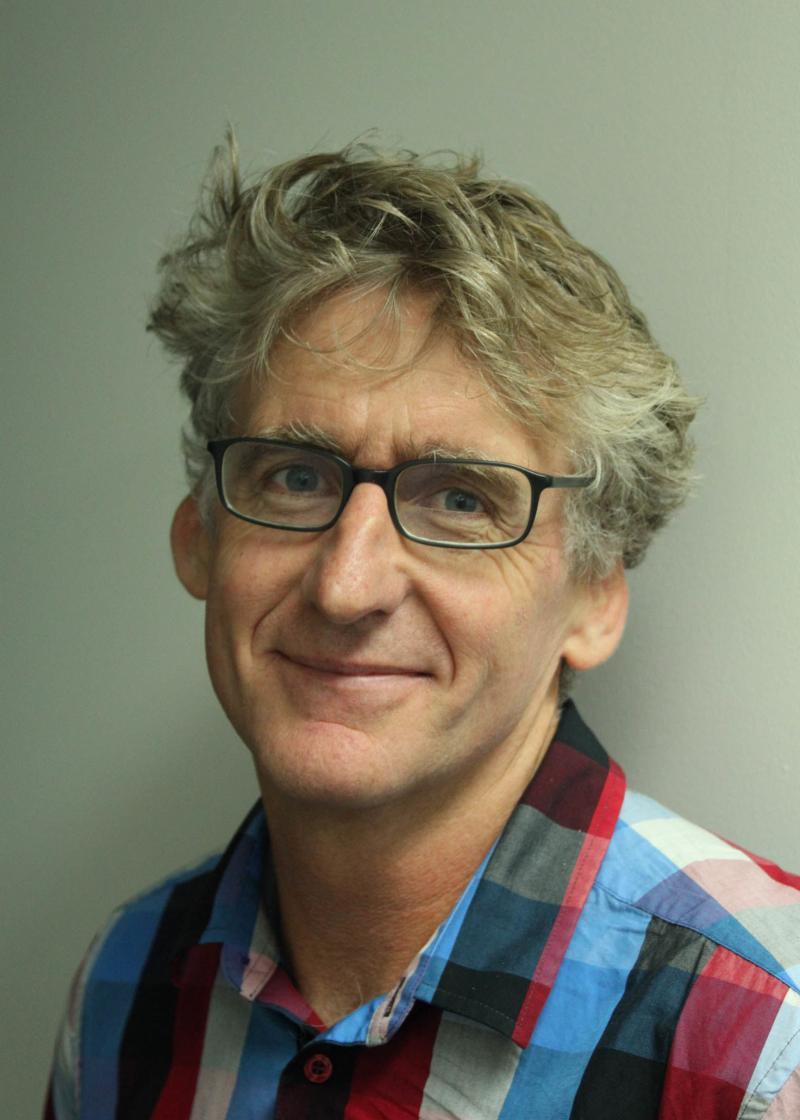 David Astle looking at the camera, smiling and wearing glasses and a chequered shirt.